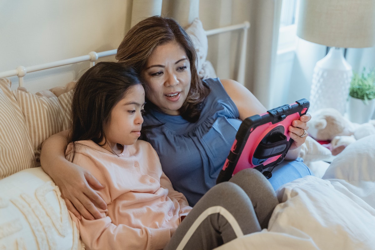 Uma mãe e sua filha na cama enquanto assistem um desenho no tablet.