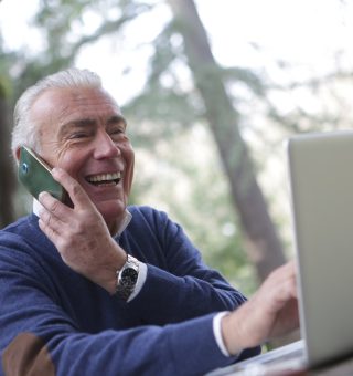 Um senhor muito feliz fazendo requerimento do INSS no notebook enquanto fala em seu celular