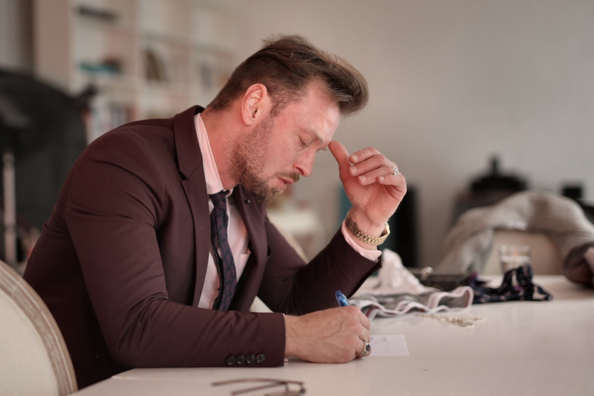 Um homem fazendo as contas o Piso INSS 2024. Ele está sentado e escreve com uma caneta. Ele apoia um dos cotovelos na mesa