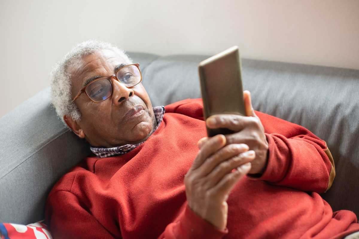 Um senhor deitado no sofá olhando para o celular, conferindo o Benefício INSS 2024 Bloqueado