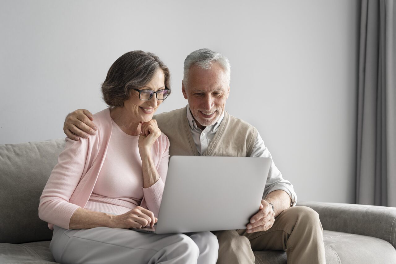 Homem e mulher aposentados analisam notícia de 13º salário em notebook