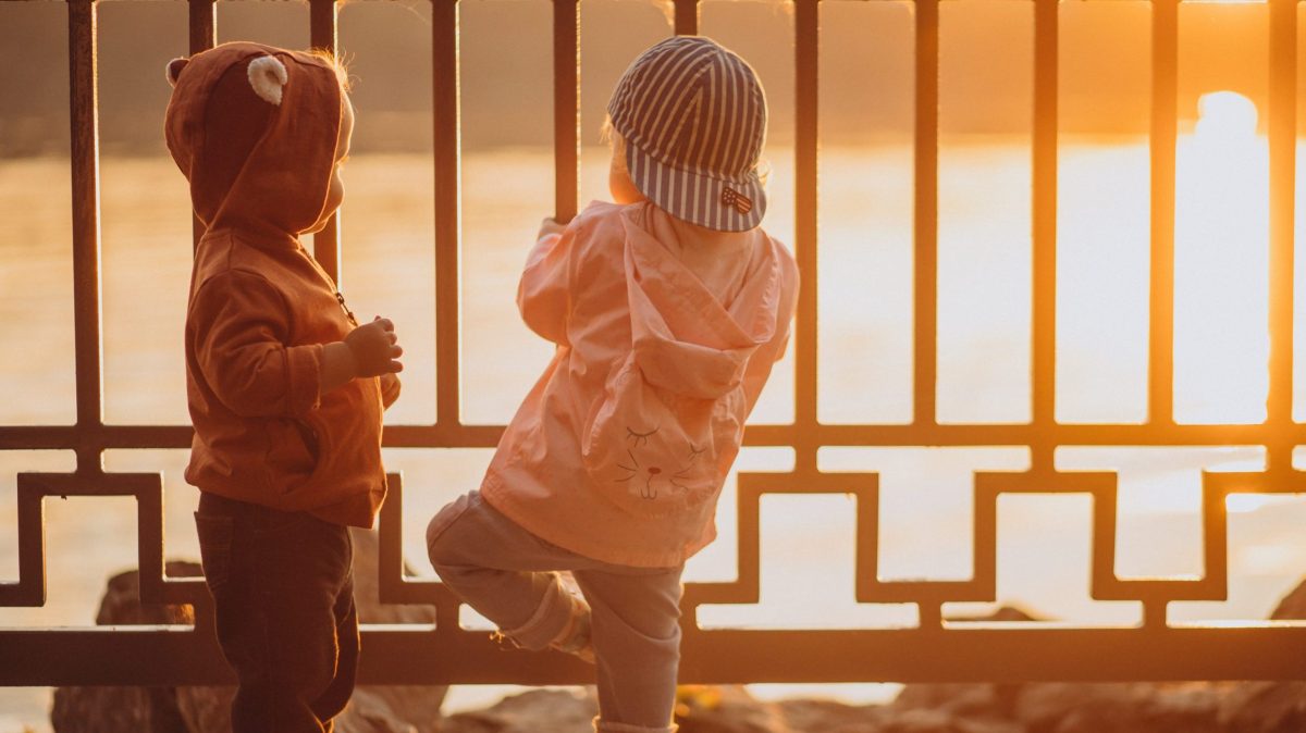 Crianças pequenas brincando em uma grade no pôr do sol